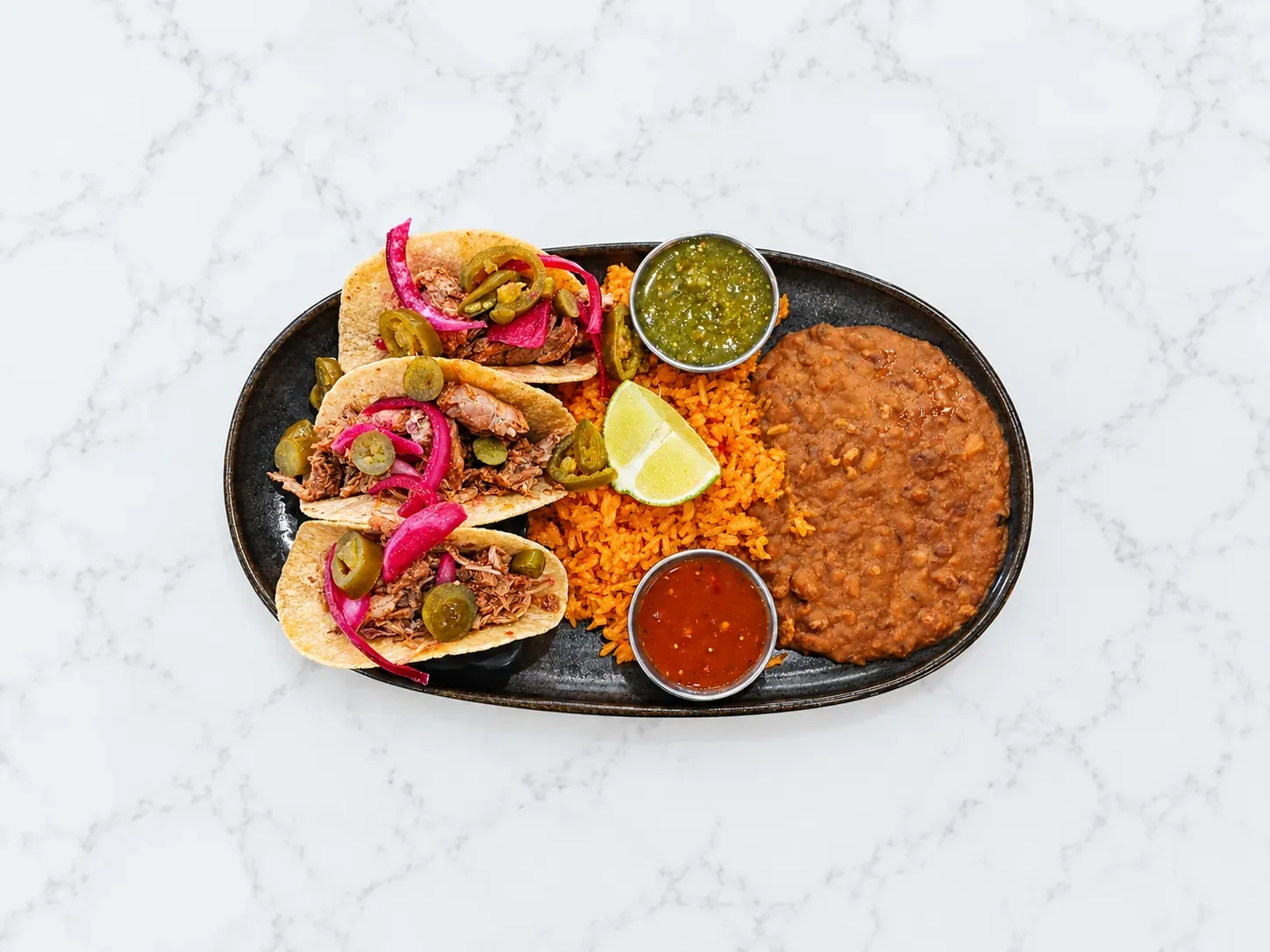 Carnitas street tacos with curtido and jalapeños, served with rice and beans