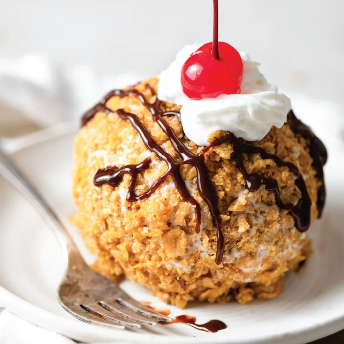 Fried ice cream with a crisp shell, chocolate drizzle, whipped cream, and a cherry